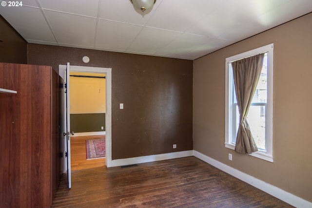 empty room with dark wood-type flooring and a drop ceiling