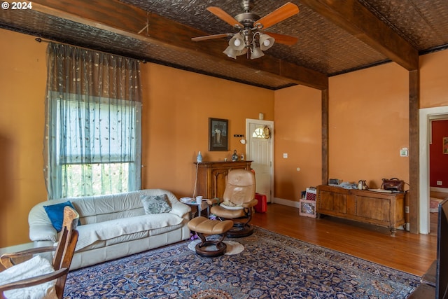 living area featuring ceiling fan, wood finished floors, baseboards, beam ceiling, and an ornate ceiling