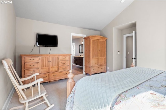 bedroom featuring ensuite bath, vaulted ceiling, and dark colored carpet