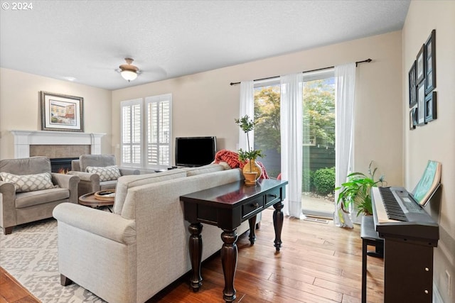 living room with a tiled fireplace, a healthy amount of sunlight, a textured ceiling, and light hardwood / wood-style floors