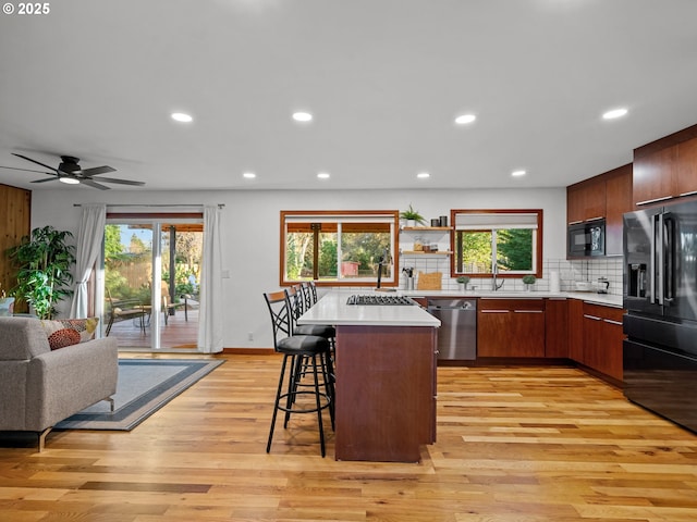 kitchen featuring a kitchen bar, light wood-type flooring, light countertops, decorative backsplash, and black appliances