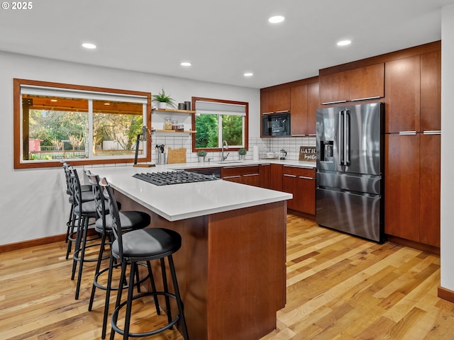 kitchen with backsplash, black microwave, a peninsula, a kitchen breakfast bar, and stainless steel refrigerator with ice dispenser