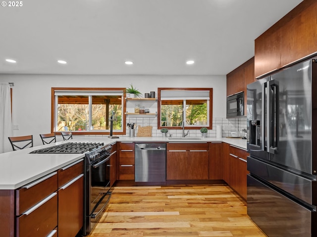 kitchen with a sink, decorative backsplash, black appliances, light countertops, and light wood-style floors