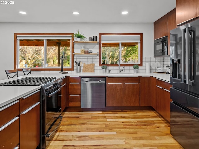 kitchen with black appliances, a sink, backsplash, light wood-style floors, and light countertops