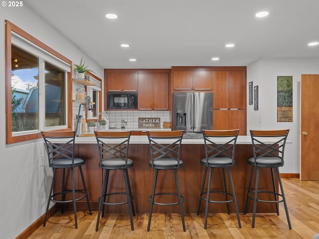 kitchen with backsplash, a peninsula, black microwave, stainless steel fridge with ice dispenser, and light countertops