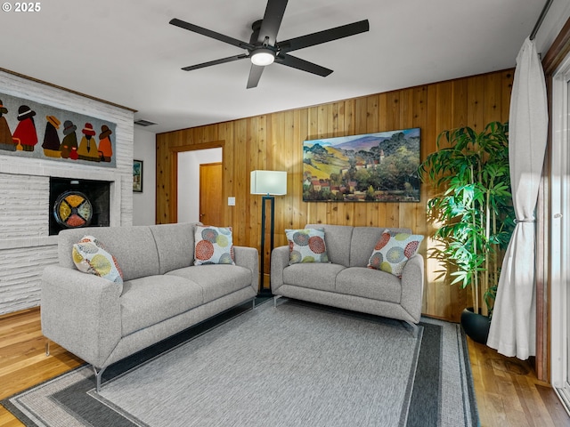 living area with visible vents, wood walls, ceiling fan, and wood finished floors