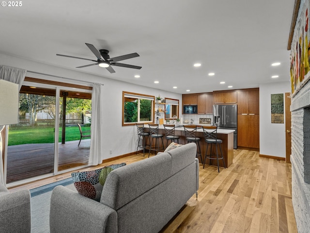 living area with a brick fireplace, recessed lighting, baseboards, and light wood finished floors