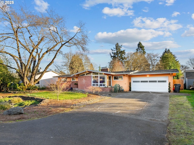 mid-century home featuring concrete driveway, an attached garage, a front lawn, and a chimney