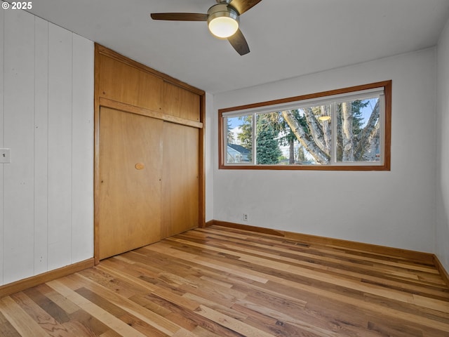 unfurnished bedroom with a closet, ceiling fan, baseboards, and light wood-style floors