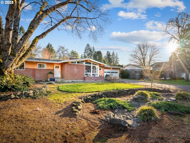 view of front of house featuring brick siding, an attached garage, driveway, and a front yard