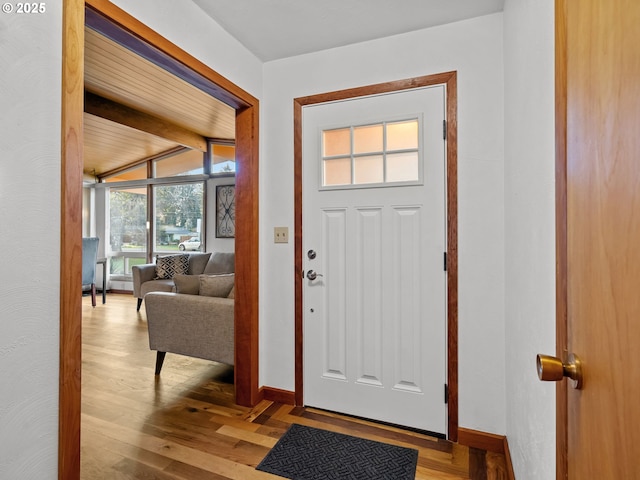 entryway with beamed ceiling, baseboards, and wood finished floors