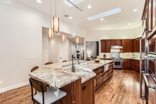 kitchen featuring a large island with sink, a kitchen breakfast bar, high end stainless steel range oven, hanging light fixtures, and sink