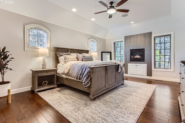 bedroom with ceiling fan, lofted ceiling, dark wood-type flooring, and a tiled fireplace