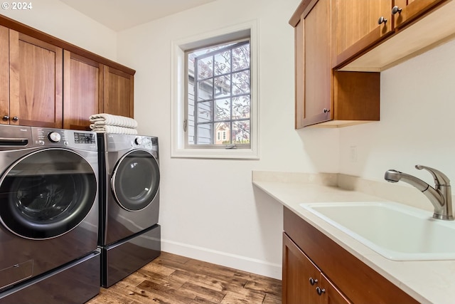 clothes washing area featuring washer and dryer, cabinets, wood-type flooring, and sink