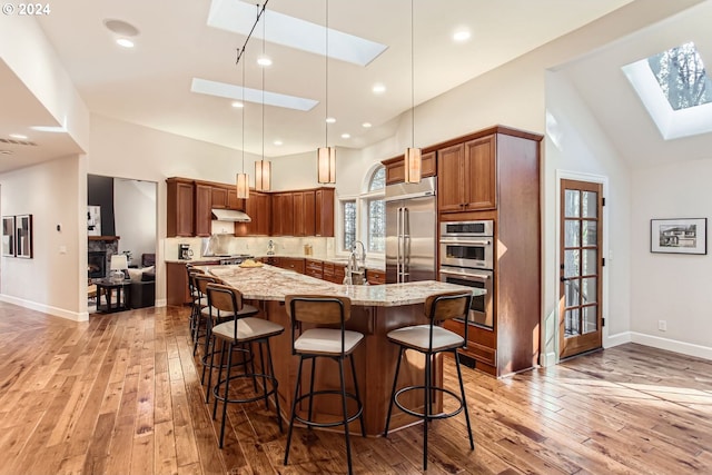 kitchen with a skylight, light stone countertops, hanging light fixtures, stainless steel appliances, and a kitchen bar