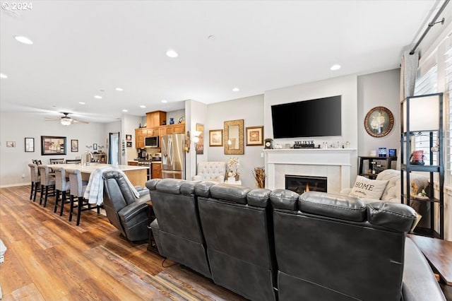 living room featuring light wood-type flooring, a tiled fireplace, and ceiling fan