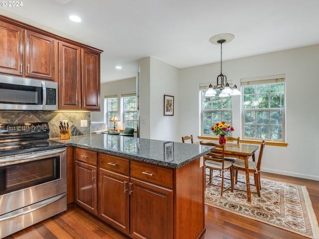 kitchen featuring tasteful backsplash, dark hardwood / wood-style floors, kitchen peninsula, dark stone countertops, and appliances with stainless steel finishes