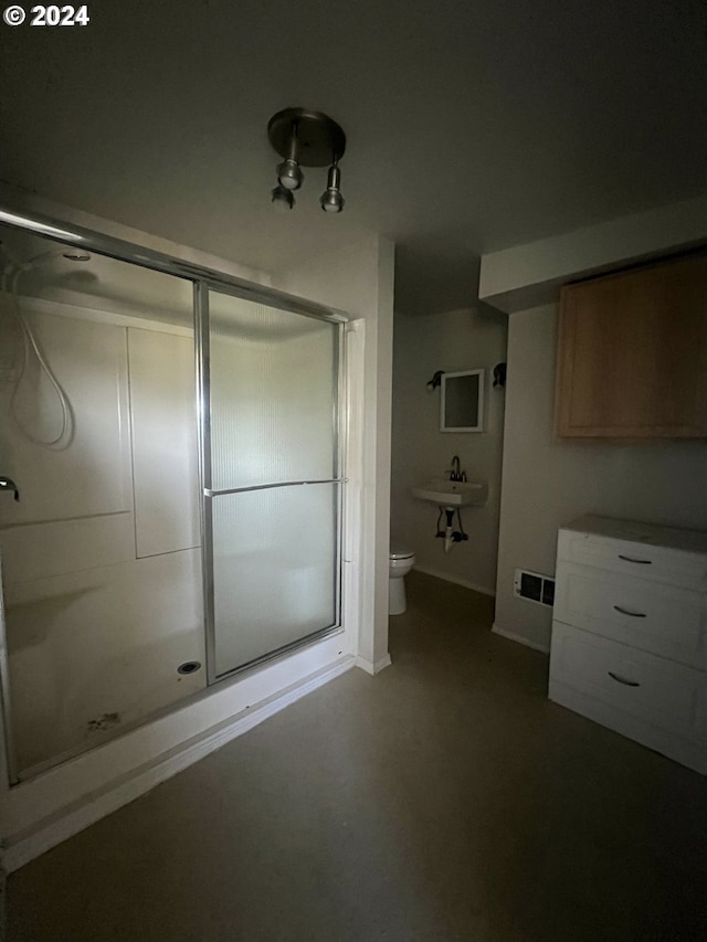 bathroom featuring toilet, a shower with door, and sink