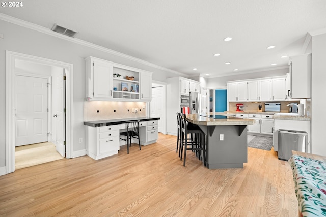 kitchen featuring white cabinetry, backsplash, light hardwood / wood-style floors, a breakfast bar, and a kitchen island