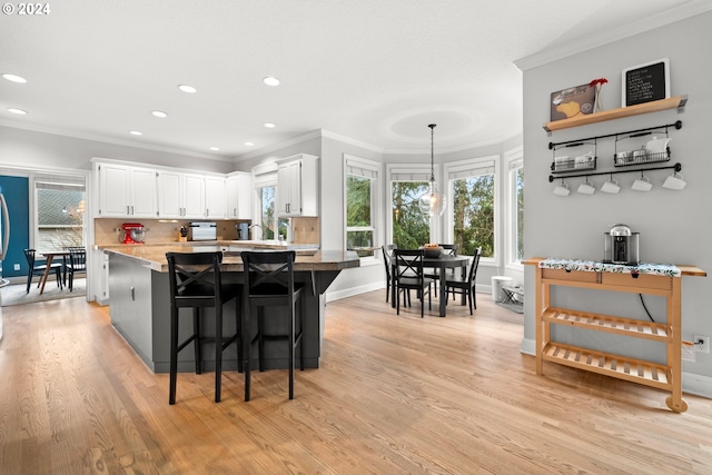 kitchen with a breakfast bar, white cabinets, crown molding, light wood-type flooring, and decorative light fixtures