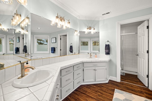 bathroom featuring a textured ceiling, tiled shower, hardwood / wood-style flooring, vanity, and ornamental molding