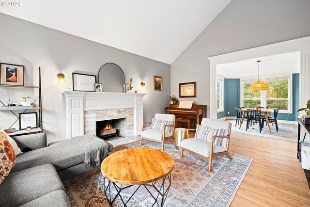 living room featuring a tiled fireplace, light hardwood / wood-style flooring, and high vaulted ceiling