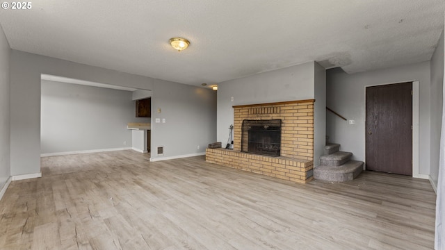 976 E St, Coos Bay, OR 97420 - unfurnished living room featuring a textured ceiling, wood finished floors, a brick fireplace, stairs, and baseboards