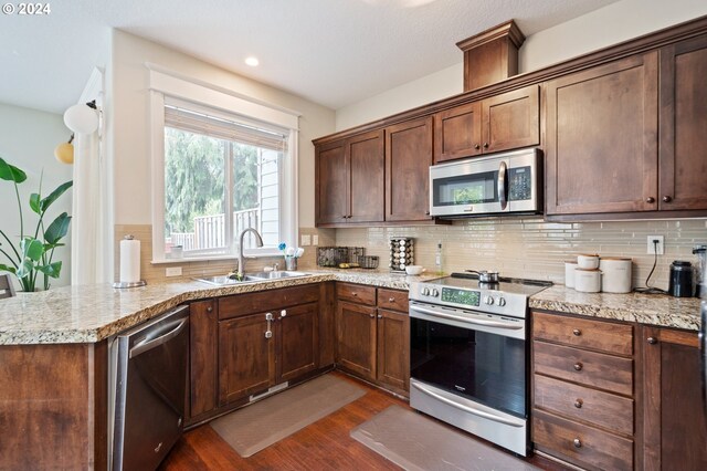 kitchen with appliances with stainless steel finishes, tasteful backsplash, sink, light stone countertops, and dark wood-type flooring