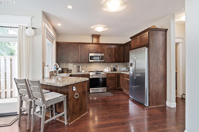 kitchen with backsplash, sink, appliances with stainless steel finishes, light stone countertops, and dark hardwood / wood-style floors