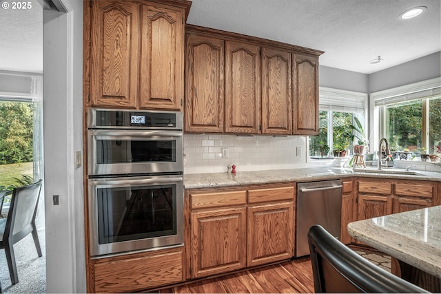 kitchen with tasteful backsplash, brown cabinets, light stone countertops, stainless steel appliances, and a sink