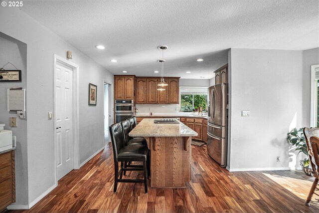 kitchen with a center island, appliances with stainless steel finishes, dark hardwood / wood-style flooring, a breakfast bar area, and a textured ceiling