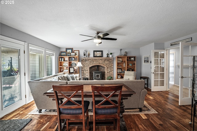 living room with a textured ceiling, dark wood-type flooring, a ceiling fan, french doors, and a wood stove