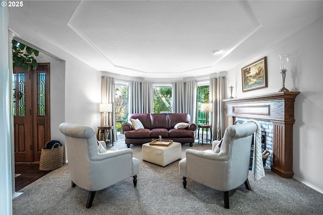 living area featuring a healthy amount of sunlight, a brick fireplace, baseboards, and a tray ceiling