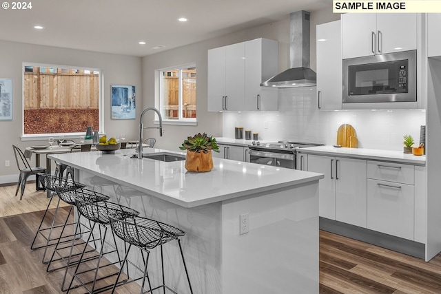 kitchen featuring an island with sink, wall chimney range hood, white cabinets, and sink