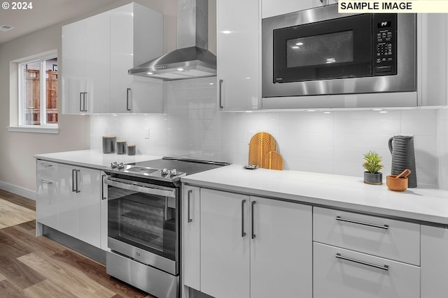 kitchen with white cabinets, built in microwave, stainless steel range with electric cooktop, and wall chimney range hood