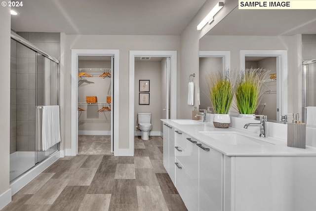 bathroom featuring wood-type flooring, toilet, vanity, and a shower with shower door