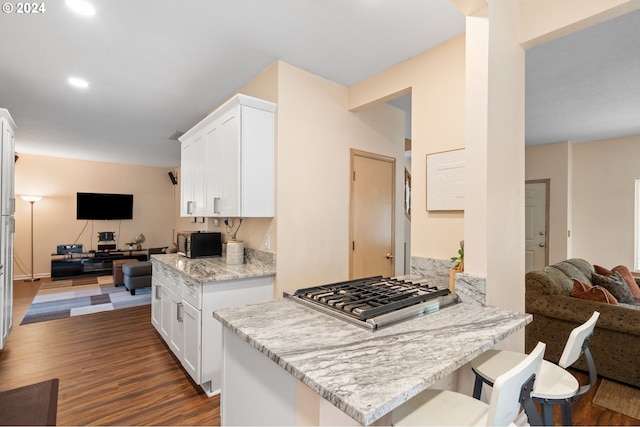 kitchen with white cabinetry, a breakfast bar area, kitchen peninsula, light stone countertops, and dark wood-type flooring