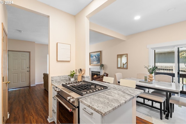 kitchen with light stone counters, dark hardwood / wood-style flooring, stainless steel stove, beam ceiling, and white cabinets