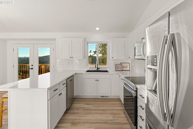 kitchen with stainless steel appliances, sink, white cabinets, vaulted ceiling, and kitchen peninsula