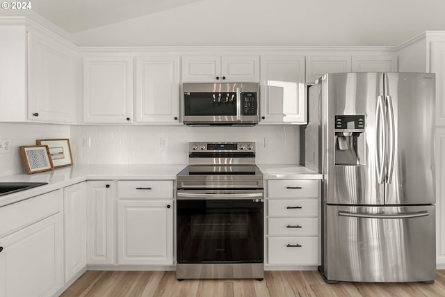 kitchen with stainless steel appliances, vaulted ceiling, white cabinets, and light hardwood / wood-style flooring