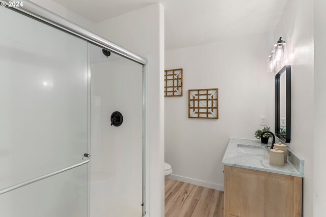 bathroom with toilet, wood-type flooring, vanity, and a shower with door