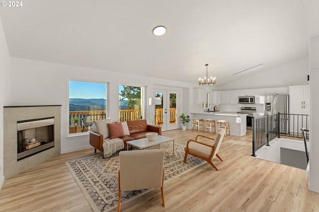 living room featuring a tiled fireplace, light wood-type flooring, a notable chandelier, a mountain view, and lofted ceiling