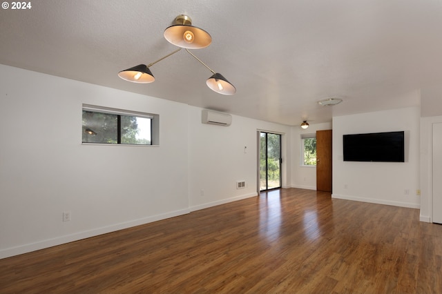 unfurnished living room with a wealth of natural light, dark hardwood / wood-style floors, and an AC wall unit