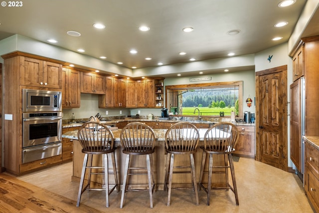 kitchen featuring appliances with stainless steel finishes, light colored carpet, a kitchen breakfast bar, and light stone countertops