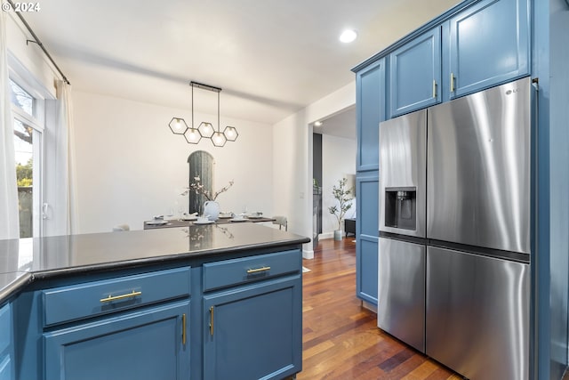 kitchen with blue cabinetry, stainless steel fridge, decorative light fixtures, and dark wood-type flooring