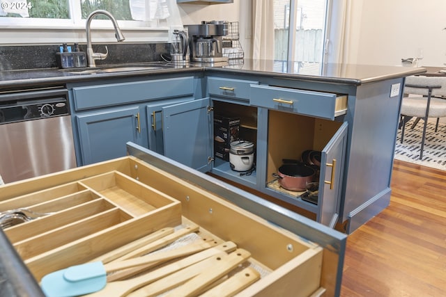 kitchen with blue cabinetry, hardwood / wood-style floors, stainless steel dishwasher, and sink