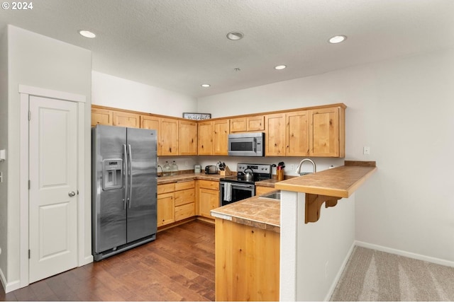 kitchen with dark hardwood / wood-style flooring, a kitchen bar, stainless steel appliances, sink, and kitchen peninsula