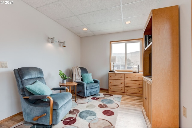 sitting room with a drop ceiling and light wood-type flooring