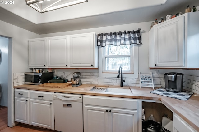 kitchen with butcher block counters, stainless steel microwave, white dishwasher, white cabinetry, and a sink