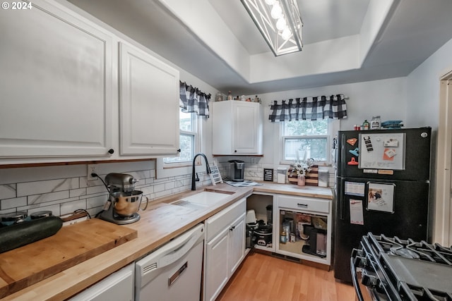 kitchen with a tray ceiling, freestanding refrigerator, white cabinetry, white dishwasher, and a sink